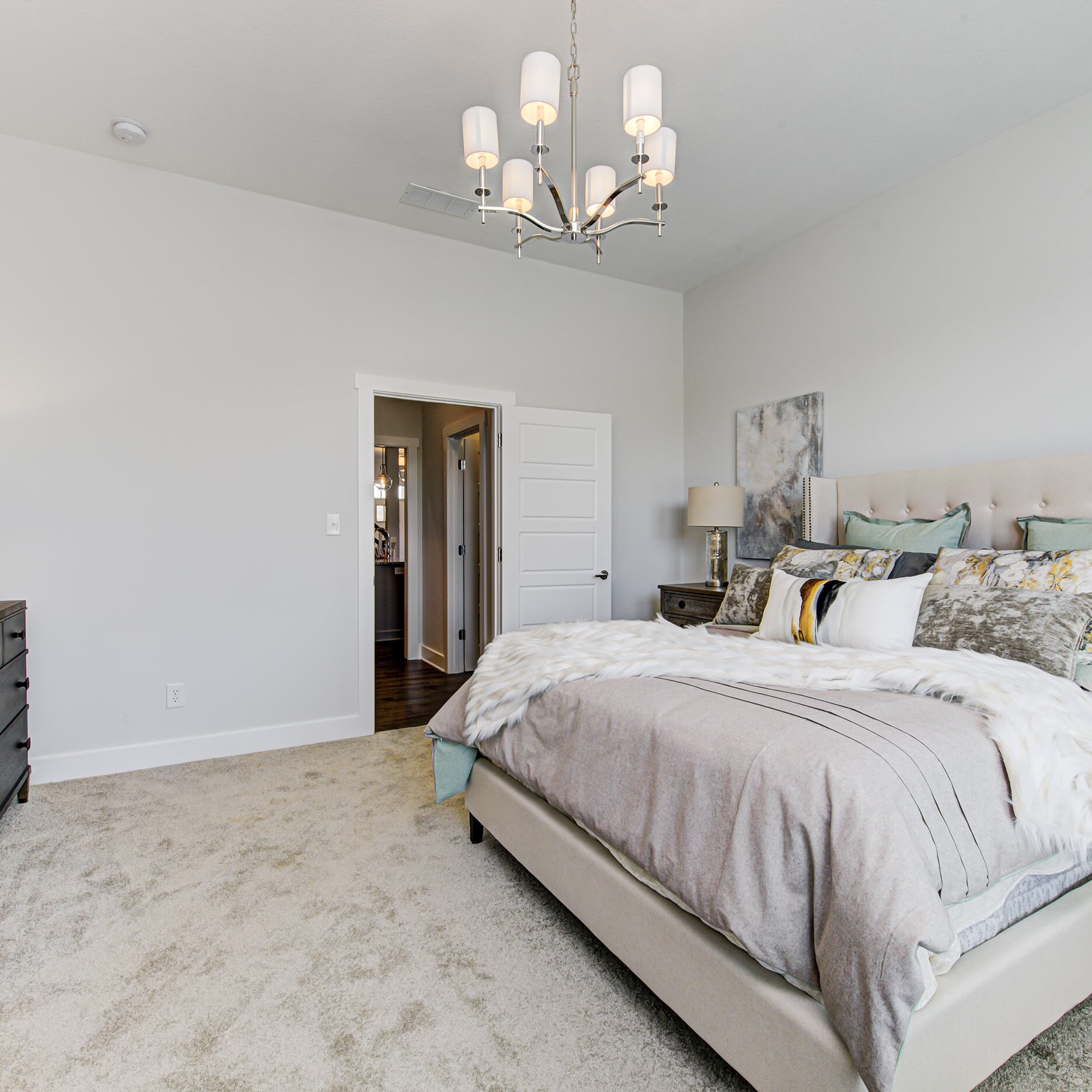 A bedroom with a bed, dresser, and a chandelier.