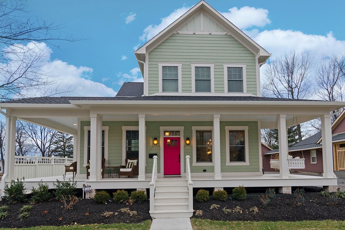 A custom home builder in Fishers, Indiana specializes in creating new homes with unique designs, one of which is a stunning green and pink house featuring a vibrant pink door.